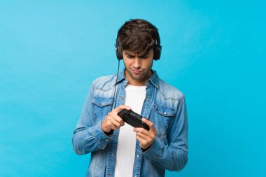 Soyutlanmış mavi arka planda video oyunlarında oynayan yakışıklı bir genç.