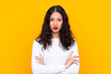 Karışık ırk kadını, izole edilmiş sarı arka planda kollarını kavuşturuyor.