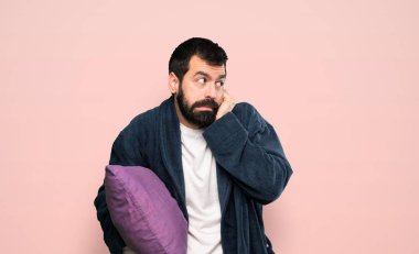 Pijamalı sakallı adam hayal kırıklığına uğramış ve pembe arka planda kulaklarını kapatmış.