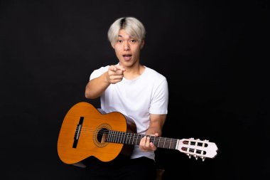 Siyah arka planda gitar çalan Asyalı genç adam şaşırdı ve ön tarafı işaret etti.