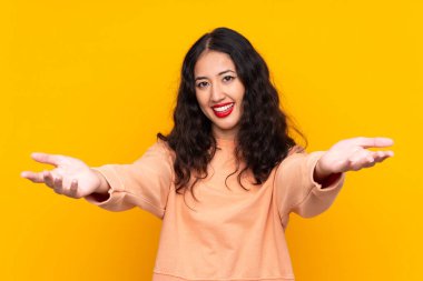 İspanyol Çinli kadın izole edilmiş sarı arka plan sunuyor ve davet ediyor.