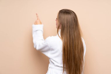 İzole edilmiş arka planda bornozlu genç kız işaret parmağıyla işaret ediyor.