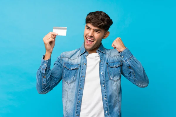 Mladý Pohledný Muž Přes Izolované Modré Pozadí Drží Kreditní Kartu — Stock fotografie