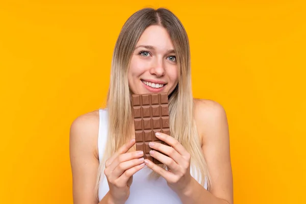 Young Blonde Woman Isolated Blue Background Taking Chocolate Tablet Happy — Stock Photo, Image