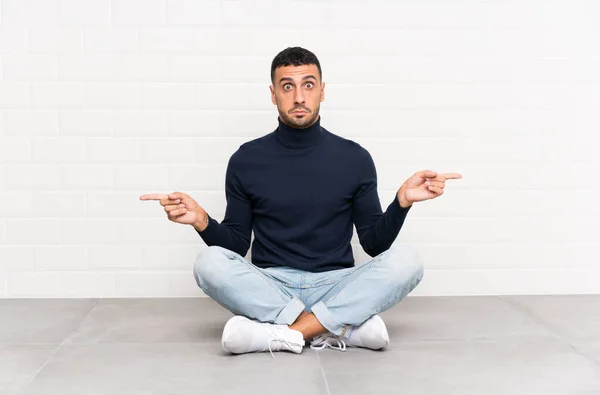 Joven Hombre Guapo Sentado Suelo Señalando Los Laterales Que Tienen — Foto de Stock