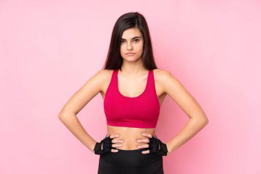 Young sport woman over isolated pink background posing with arms at hip