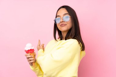 Genç esmer kız izole edilmiş pembe arka plan üzerinde kornet dondurması tutuyor.