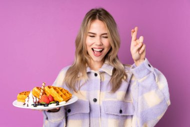 Elinde waffle tutan genç Rus kız mor arka planda izole edilmiş ve şans diliyor.