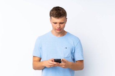 İzole edilmiş beyaz arka planda genç yakışıklı bir adam cep telefonuyla mesaj gönderiyor.
