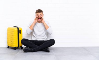 Genç yakışıklı bir adam bavulla yerde oturuyor ve ağzı açık bağırıyor.