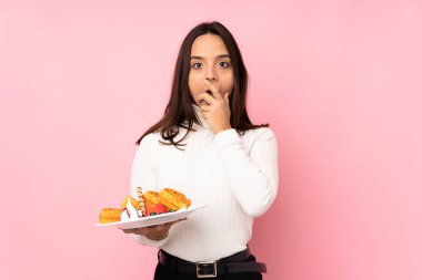 Koyu pembe arka planda waffle tutan genç esmer kadın sağa bakarken şaşırmış ve şok olmuştu.