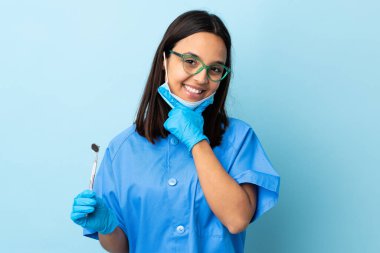 Genç, esmer, melez bir dişçi kadının elinde izole edilmiş arka planda mutlu ve gülümseyen aletler var.