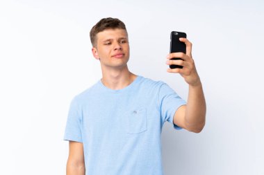Soyutlanmış beyaz arka planda genç yakışıklı bir adam selfie çekiyor.