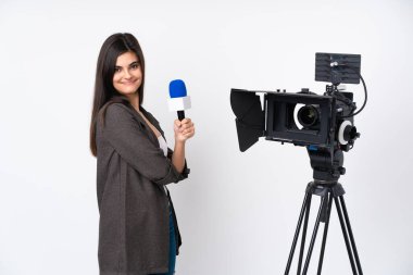 Muhabir kadın mikrofon tutuyor ve beyaz arka planda gülüp haber veriyor.