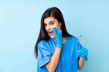 İzole edilmiş mavi arka plan üzerinde aletleri tutan genç dişçi bir şey fısıldıyor.