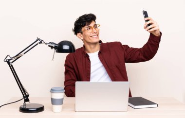 Masadaki genç Arjantinli adamın iş yerinde dizüstü bilgisayarı var.