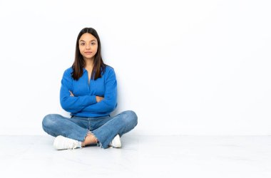 Genç melez kadın, arka planda beyaz arka planda izole bir şekilde yerde oturuyor.