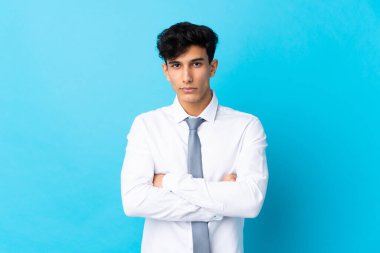 Genç Arjantinli iş adamı mavi arka planda kollarını kavuşturuyor.