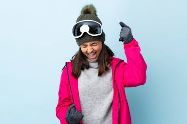 Karma kayakçı kız, snowboard gözlükleriyle izole edilmiş mavi arka planda zaferi kutluyor..