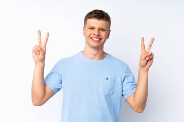 İzole edilmiş beyaz arka planda genç yakışıklı adam iki eliyle zafer işareti gösteriyor.