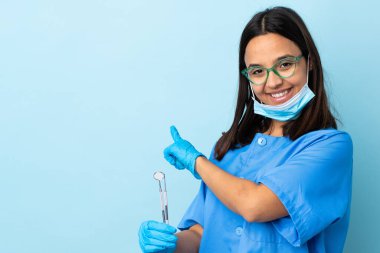 Genç, esmer, melez bir dişçi kadının elinde izole bir arka plan üzerinde aletler var.