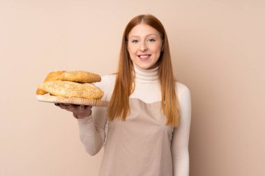 Şef üniformalı genç kızıl saçlı kadın. Kadın fırıncı elinde birkaç ekmeğin bol bol gülümsediği bir masa tutuyor.