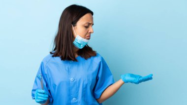 Genç, esmer, melez, dişçi kadının elinde izole edilmiş arka plan üzerinde araçlar var. Kopyalama alanını şüpheyle tutuyor.