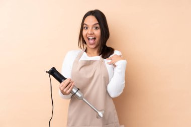 Genç esmer kız, el blendırı kullanıyor. İzole edilmiş arka planda, şaşırmış yüz ifadesi var.