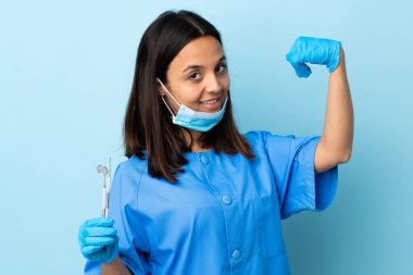 Genç, esmer, melez, dişçi kadın izole arka planda aletler tutuyor güçlü jestler yapıyor.