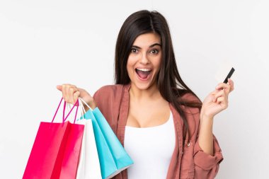 Soyutlanmış beyaz arka planı olan genç bir kadın alışveriş torbaları tutuyor ve şaşırıyor.