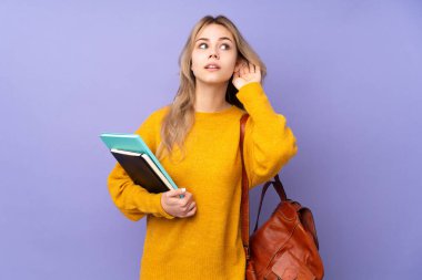 Mor arka planda izole edilmiş genç Rus öğrenci elini kulağına koyarak bir şeyler dinliyor.