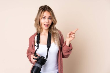 İzole edilmiş arka planda genç fotoğrafçı kız parmak uçlarını işaret ediyor ve mutlu.