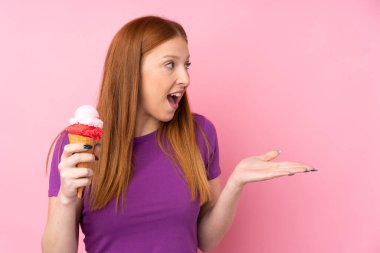 Kornet dondurması olan genç kızıl saçlı kadın izole edilmiş pembe bir arka plan ve şaşırtıcı bir yüz ifadesi var.