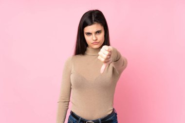 Soyutlanmış pembe arka planda genç bir kadın, olumsuz bir ifadeyle baş parmağını aşağı gösteriyor.