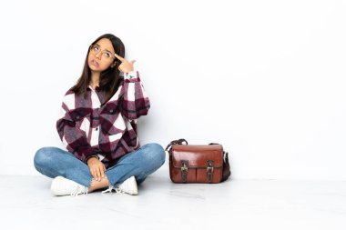 Genç bir bayan öğrenci yerde oturuyor. Delilik jesti yapıyor. Parmağını kafaya koyuyor.