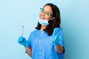 Genç, esmer, melez bir dişçi kadının elinde izole edilmiş arka planda parmak kaldırma ve gösterme araçları var.