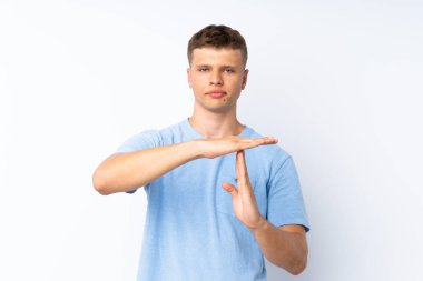 Soyutlanmış beyaz arka planda genç yakışıklı bir adam zaman aşımı hareketi yapıyor.