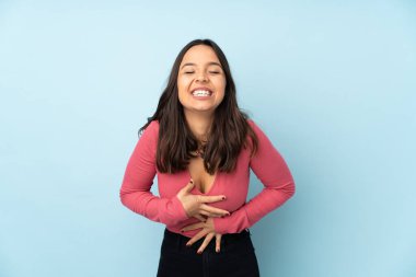 Genç melez kadın mavi arka planda izole edilmiş, çok gülümsüyor.