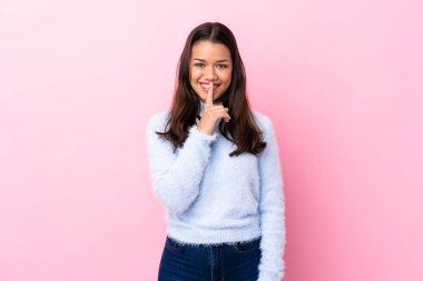 Soyutlanmış pembe arka planda genç Kolombiyalı kız sessizlik hareketi yapıyor.