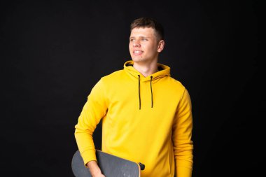 Yakışıklı genç kaykaycı, izole edilmiş siyah duvarın üstünde.