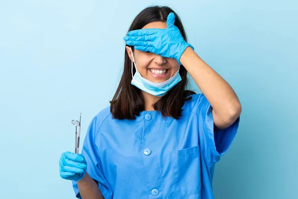 年轻的黑发混血女牙医手拿工具遮住孤立的背景 用手捂住眼睛 微笑着 — 图库照片