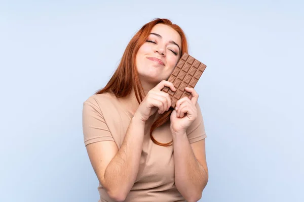 Redhead Teenager Dívka Přes Izolované Modré Pozadí Čokoládovou Tabletu Šťastný — Stock fotografie