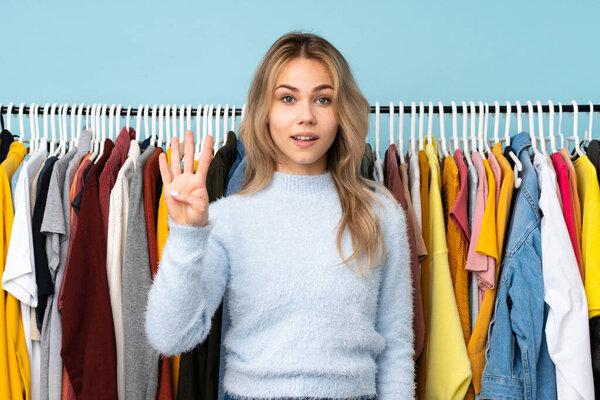 Teenager Russian girl buying some clothes isolated on blue background happy and counting four with fingers