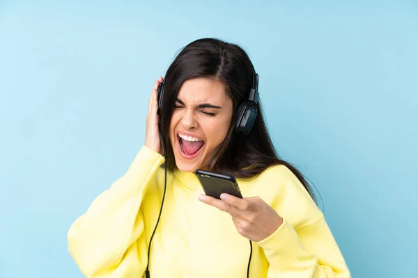 Jovem Sobre Fundo Azul Isolado Ouvindo Música Com Celular Cantando — Fotografia de Stock