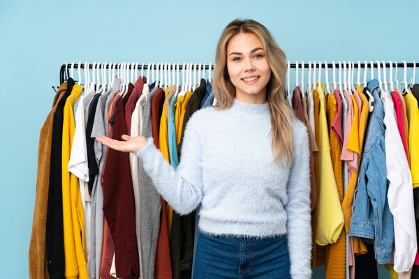 Teenager Russian girl buying some clothes isolated on blue background holding copyspace imaginary on the palm to insert an ad