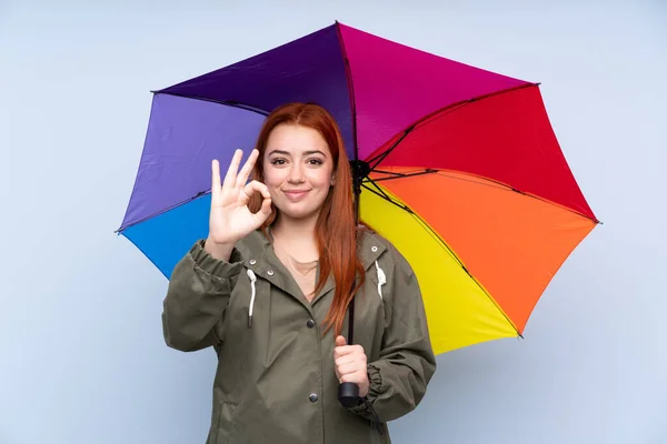 Rotschopf Teenager Mädchen Mit Einem Regenschirm Über Isolierten Blauen Hintergrund — Stockfoto