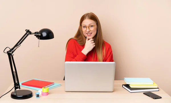 Young student woman in a workplace with a laptop with glasses and smiling