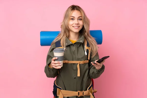 十代のロシアの登山家の女の子とともに大きなバックパック隔離された上ピンクの背景保持コーヒーへ取り去ると携帯電話 — ストック写真