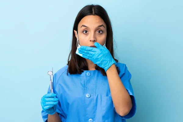 年轻的黑发混血女牙医手拿着工具盖住孤立的背景盖住嘴 — 图库照片