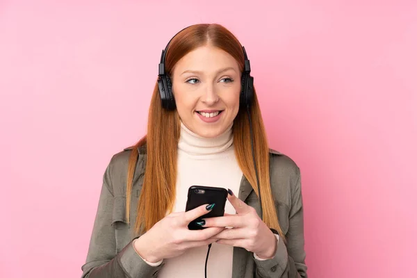 Νεαρή Κοκκινομάλλα Γυναίκα Πάνω Από Απομονωμένη Ροζ Φόντο Ακούγοντας Μουσική — Φωτογραφία Αρχείου